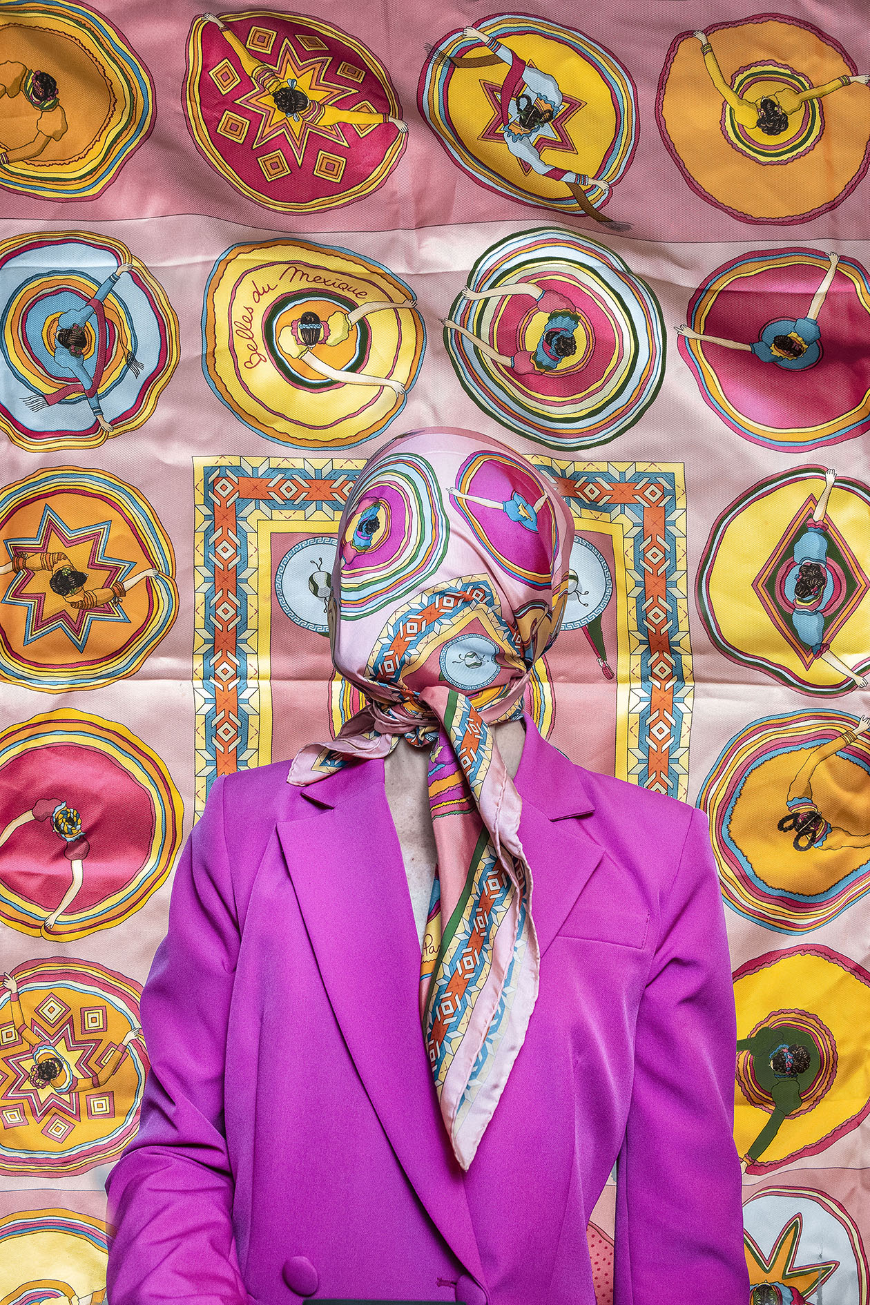 Color Cover — staged self-portrait of a figure in a fuchsia suit with a printed silk scarf covering the face, standing before a wall of the same vibrant scarf design
