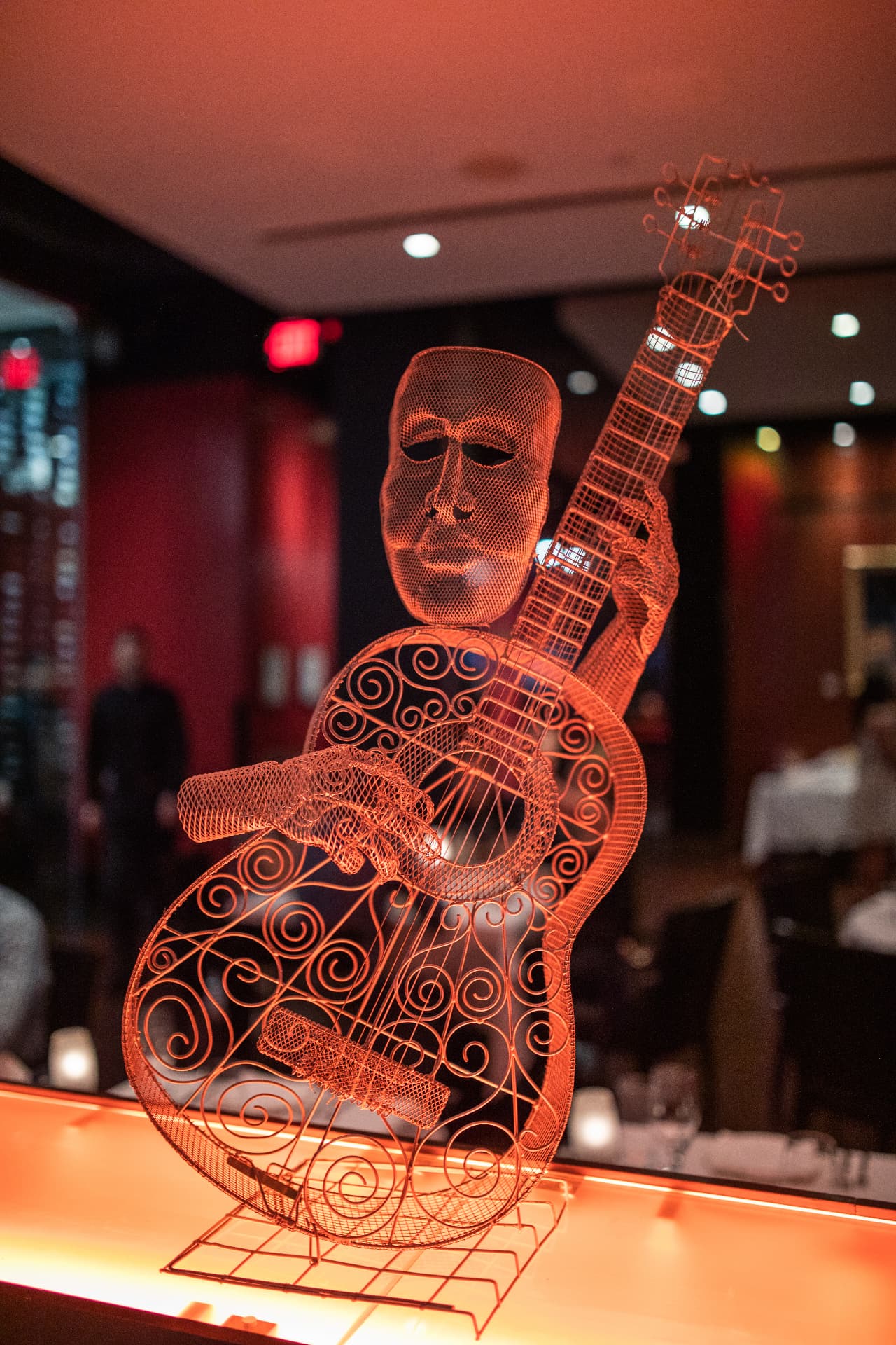 Wire-mesh guitarist sculpture bathed in amber light, art staged in a luxury restaurant
